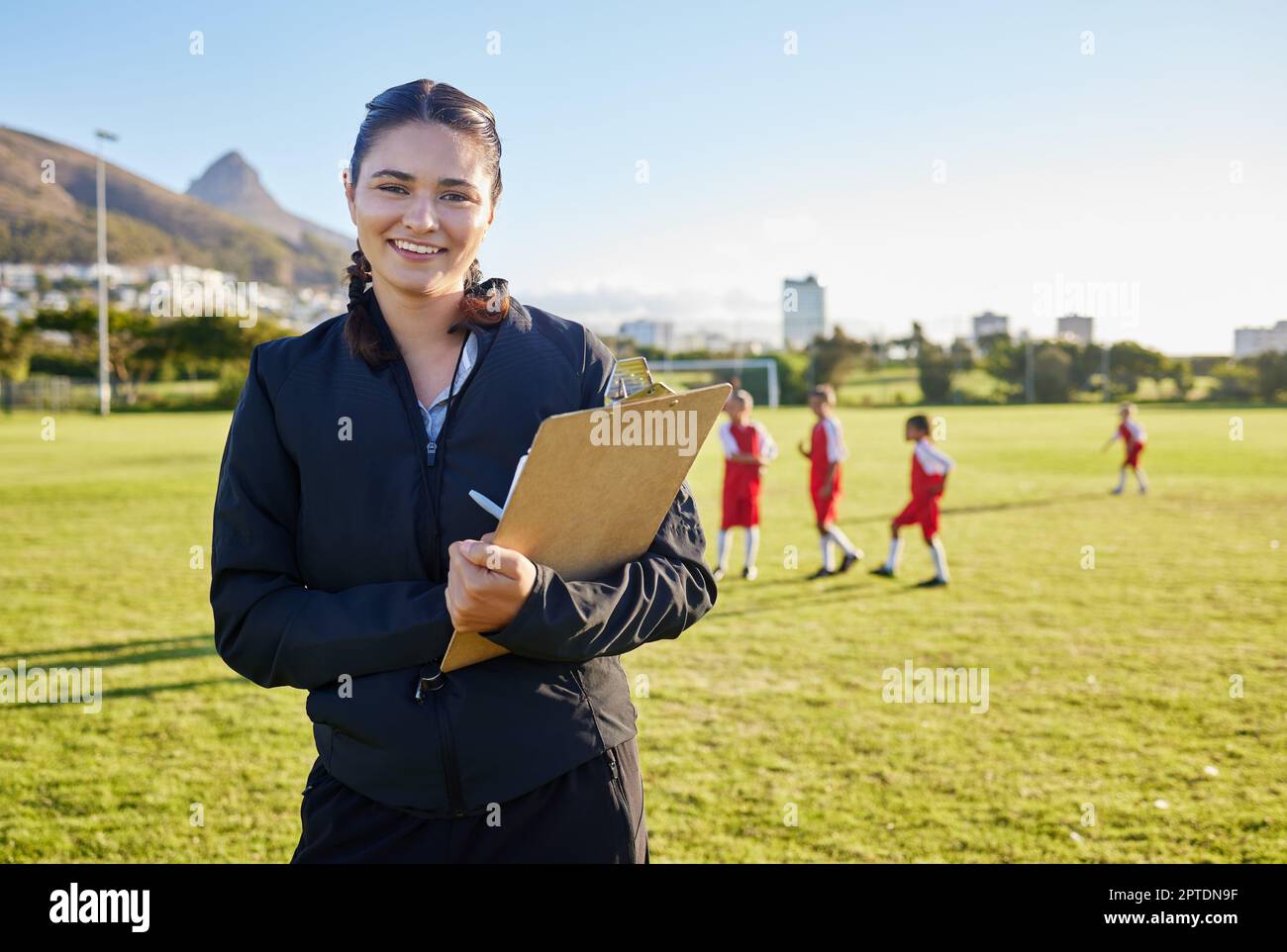 Football coach, junior sports and woman with clipboard coaching children on a soccer field or pitch outside on a sunny day. Happy female pe trainer ou Stock Photo