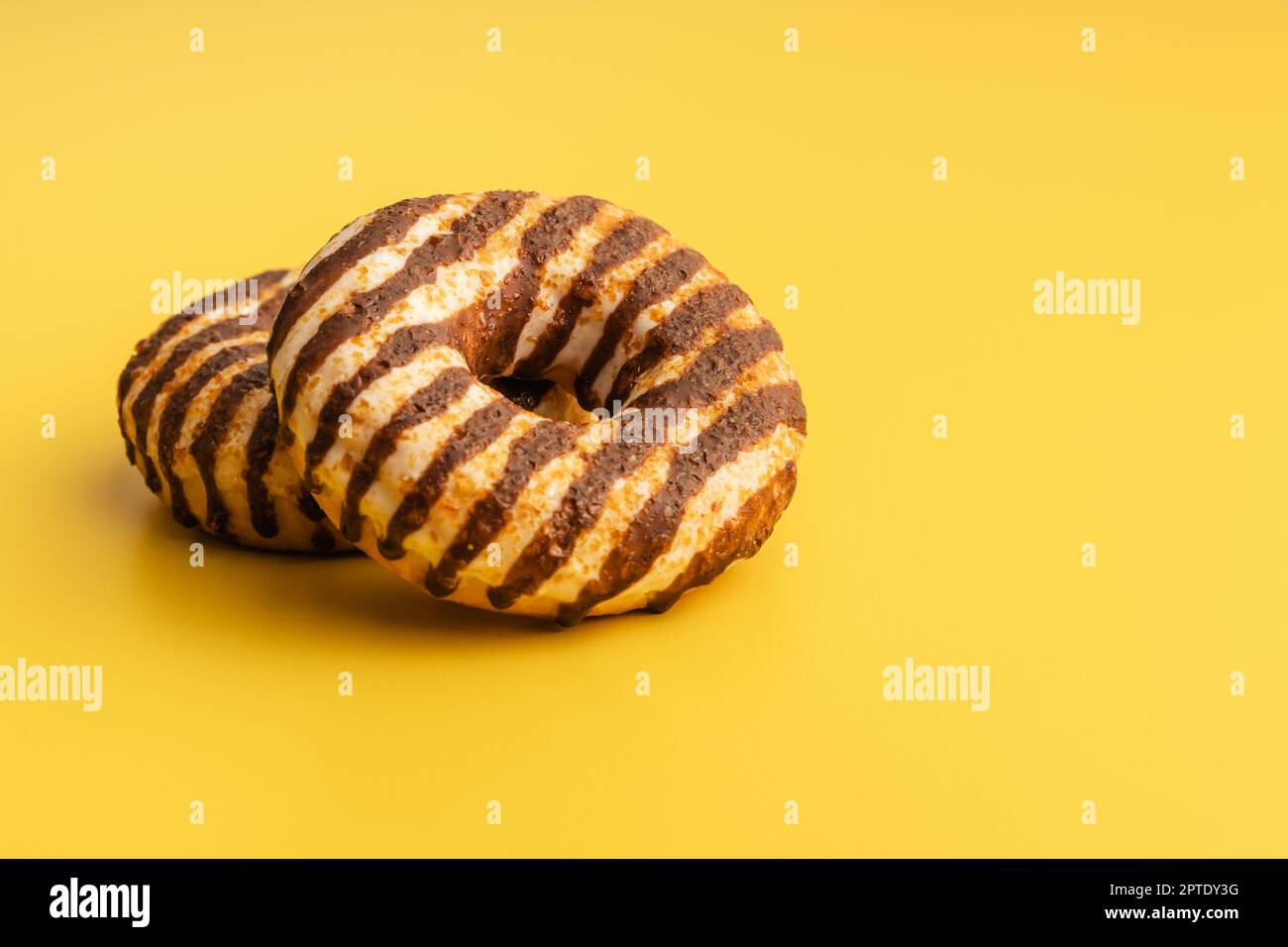 Donut with chocolate and caramel icing on the yellow background. Stock Photo