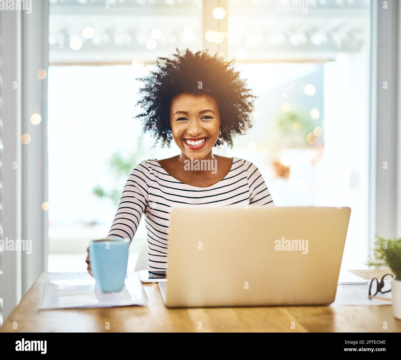 No stress when youre your own boss. Portrait of a cheerful young woman working on a laptop and drinking coffee while looking at the camera at home Stock Photo