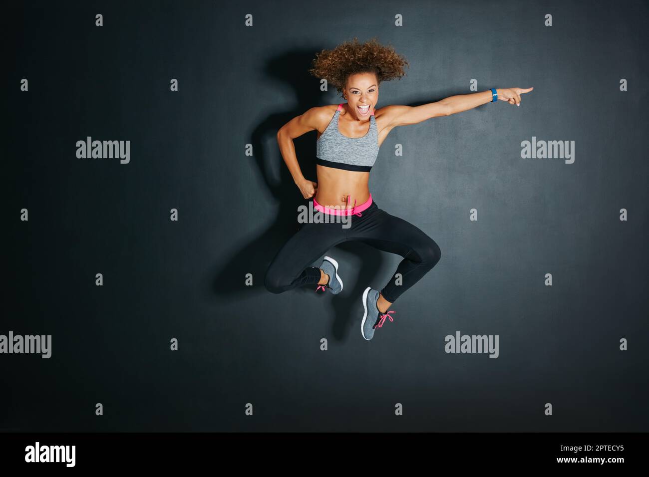 Dont look back, youre not going that way. a sporty young woman jumping against a grey background Stock Photo