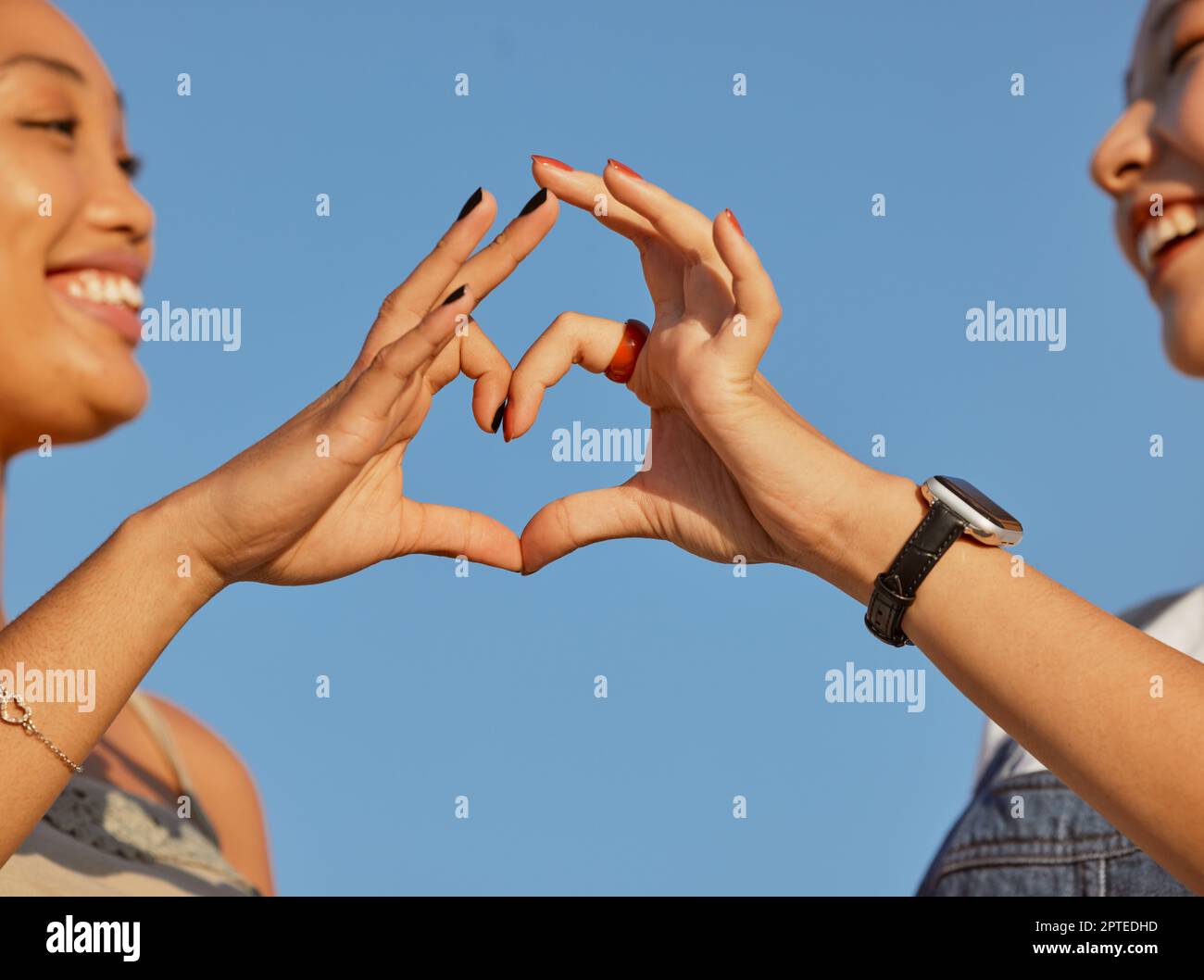 Heart, love and friends with a sign of their support, trust and happy against a blue sky. Nature, care and women with emoji hands for travel natural e Stock Photo