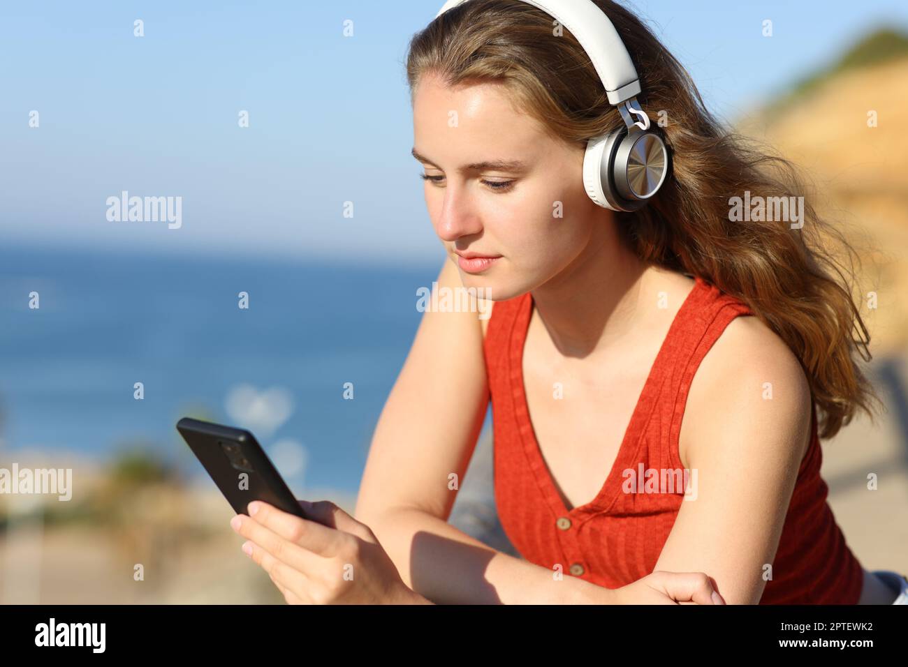 Teen on the beach with headphones listening to music checking phone
