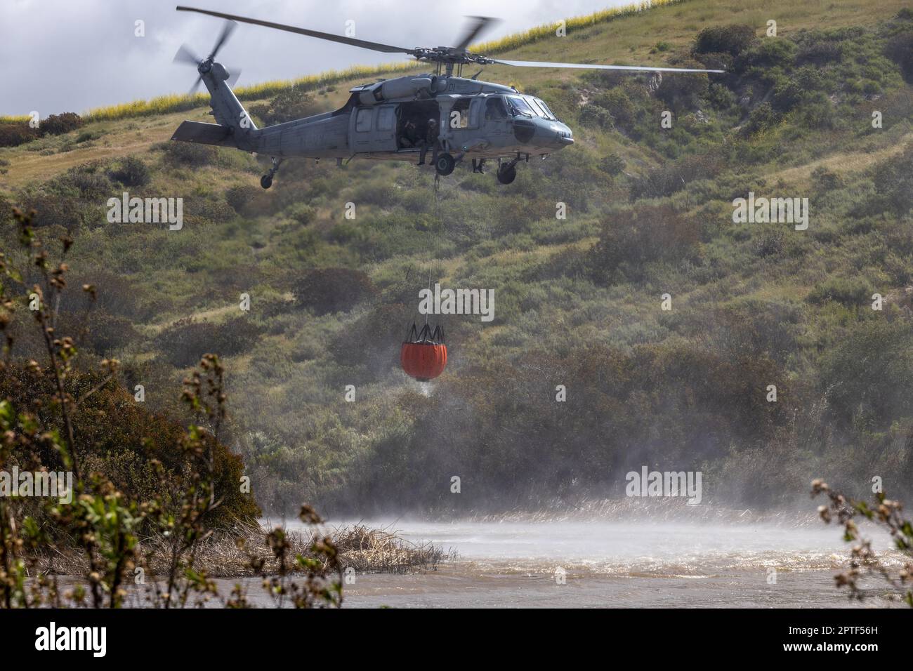 A U.S. Navy SH-60 Sea Hawk helicopter fills a bambi bucket with water during the annual Cory Iverson Wildland Firefighting exercise at the Las Pulgas Lake on Marine Corps Base Camp Pendleton, California, April 19, 2023. The Cory Iverson Wildland Firefighting exercise is an annual event that focuses on interagency cooperation between the California Department of Forestry and Fire Protection, San Diego County Sheriff's Department, and the Department of Defense. During the exercise, each entity works together to create an effective, efficient, and well trained team to respond in the event of Wild Stock Photo