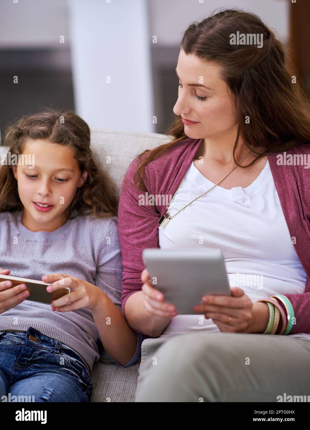 What you got there. a young girll and her mother sitting on the sofa and using their smart devices Stock Photo