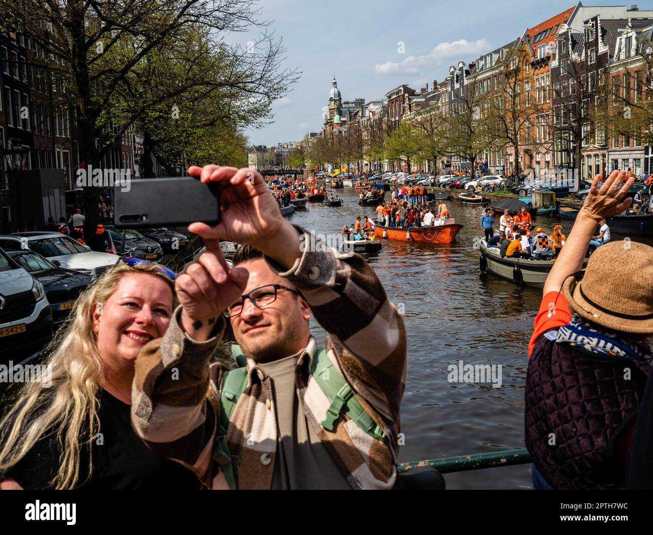 Amsterdam, Netherlands. 27th Apr, 2023. A couple is seen taking a selfie with the boats sailing on the canals. King's Day is renowned for being one of the biggest and most colorful festivities in the country, especially in Amsterdam. The city is bursting with orange as people enjoy the biggest street party of the year, enjoying the free markets and having fun on the boats along the canals. (Photo by Ana Fernandez/SOPA Images/Sipa USA) Credit: Sipa USA/Alamy Live News Stock Photo