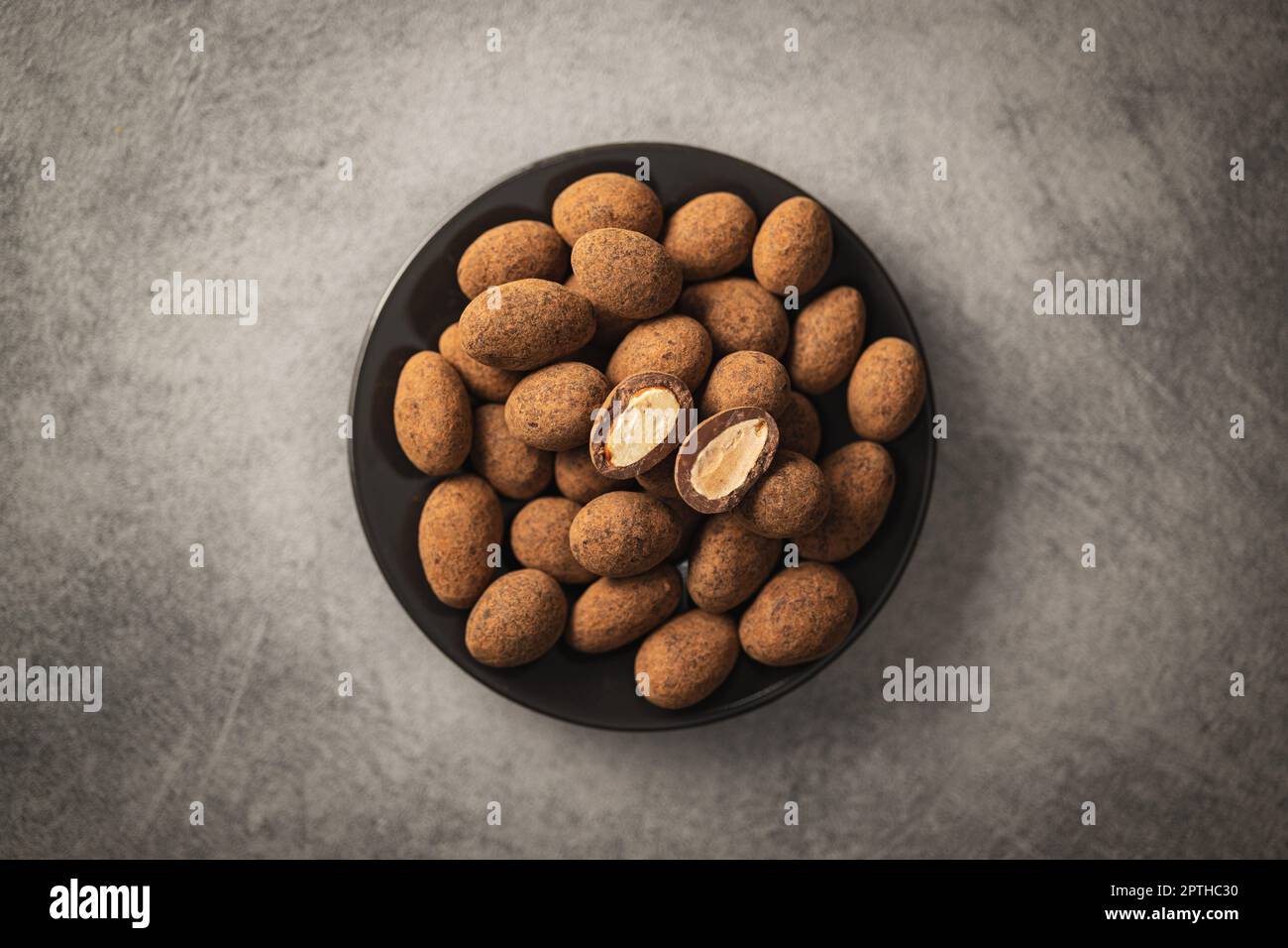 Almonds in chocolate coated in cocoa in bowl on a dark table. Top view. Stock Photo