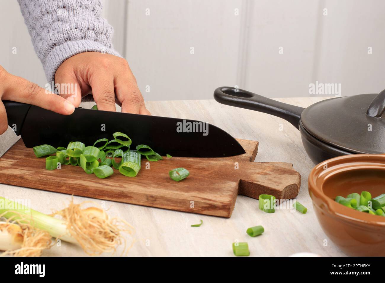Female Hand Slicing Green Onion on Wooden Choppingboard using Black Knife. Cooking Backstage Stock Photo