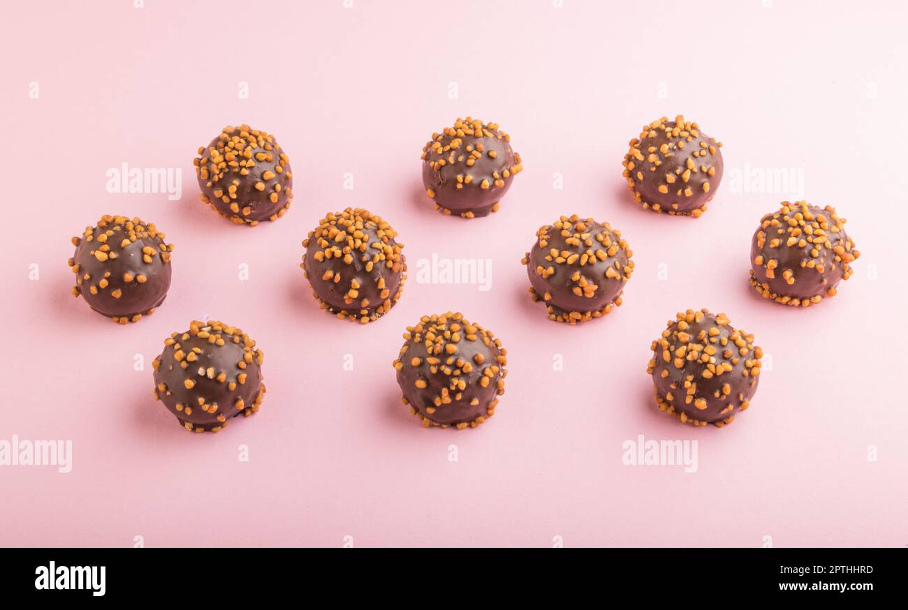 Chocolate caramel ball candies with almonds in a row on a pastel pink