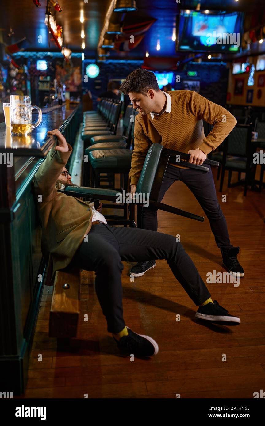 Fight in a pub. Angry guy pulling friend with chair. Aggression and conflict concept. Hooligans confrontation at sport bar Stock Photo