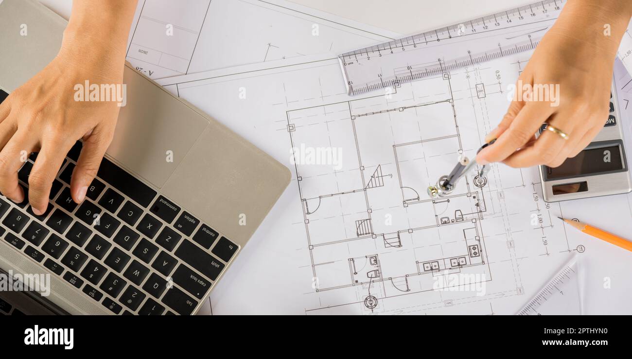 Architectural project workplace. Architect typing laptop keyboard to review design of house before editing or sketching with compass on plan blueprint Stock Photo