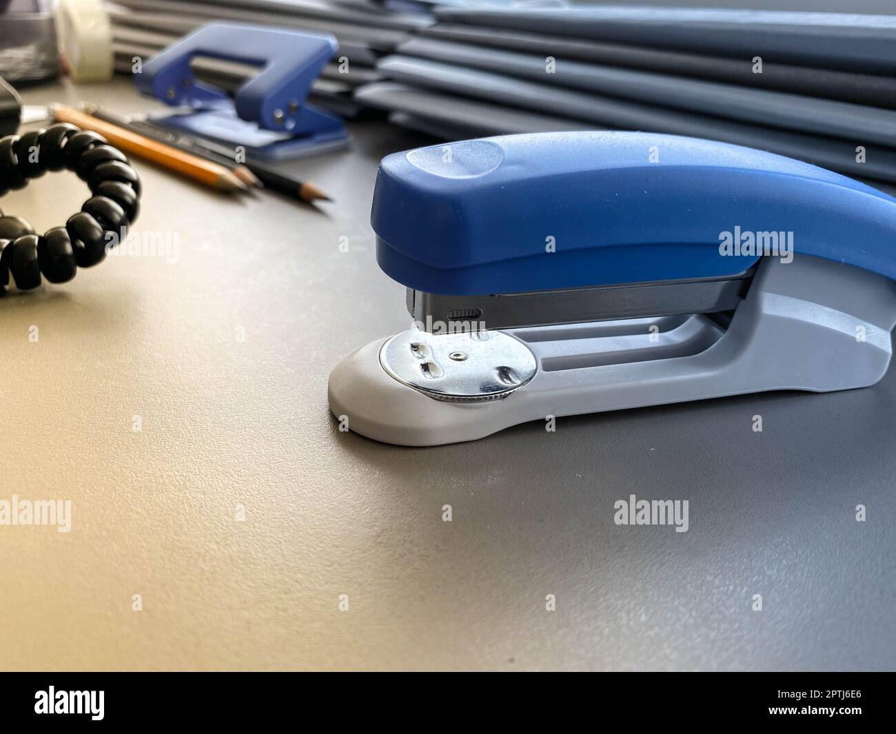 A large blue stapler for stapling paper lies next to the folders of ...