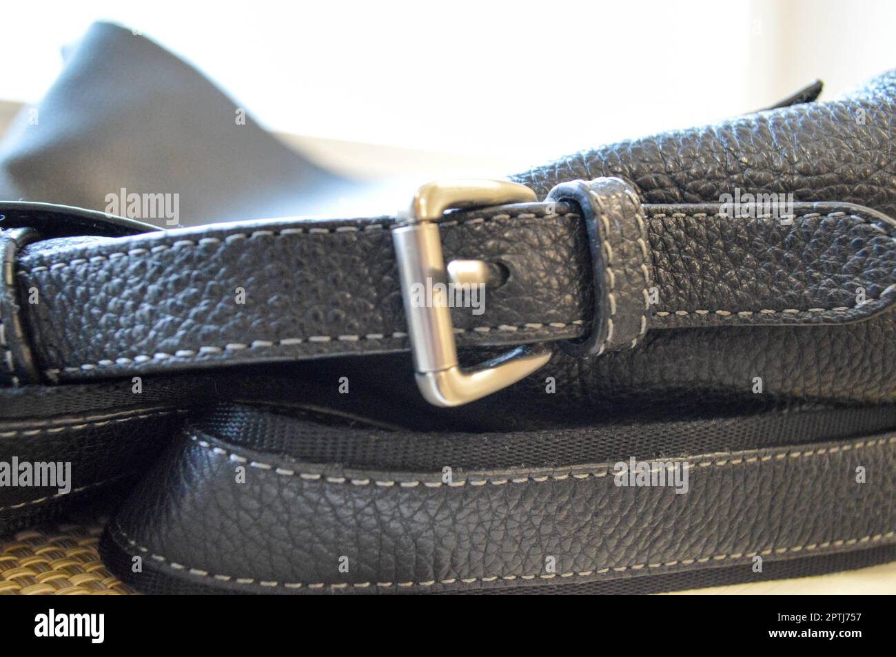 Metal buckle, clasp on a black leather belt sewn with white thread