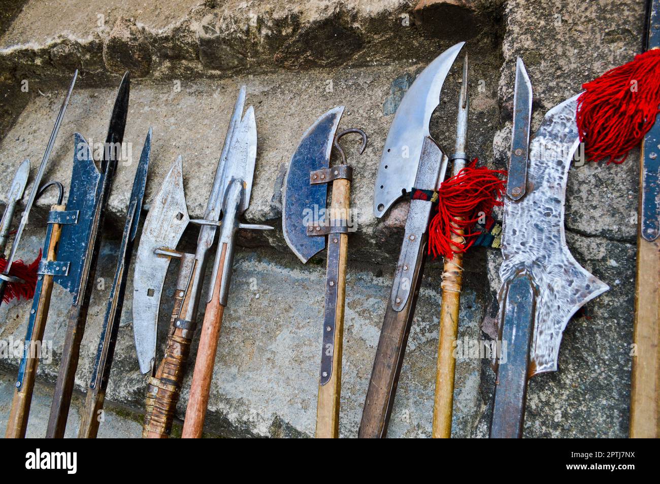 The old ancient medieval cold weapons, axes, olibards, knives, swords with wooden handles lick on the stone steps of the castle. Stock Photo
