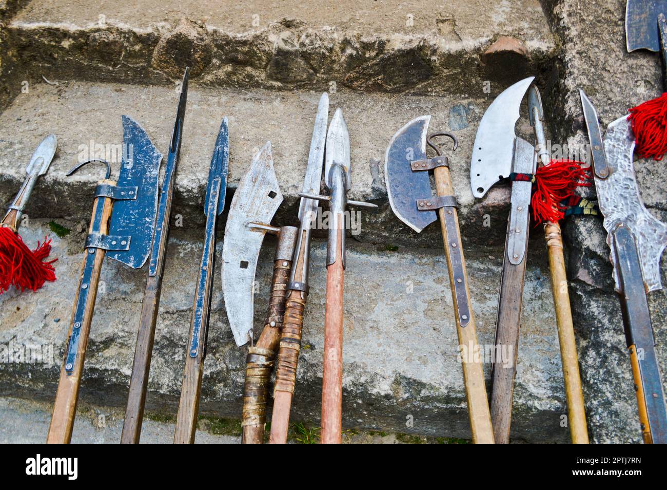 The old ancient medieval cold weapons, axes, olibards, knives, swords with wooden handles lick on the stone steps of the castle. Stock Photo