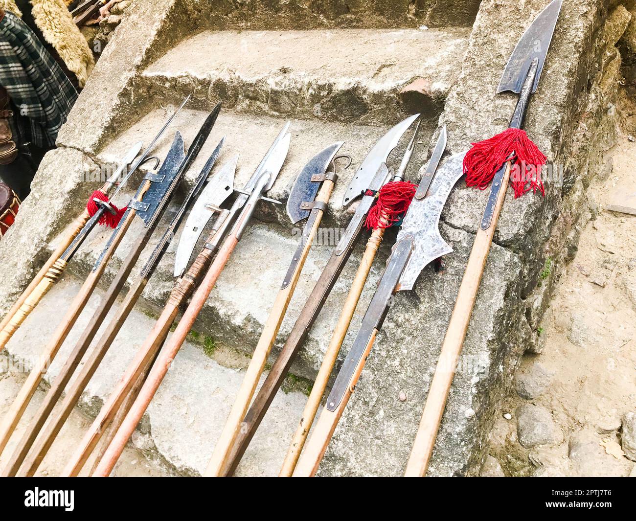 The old ancient medieval cold weapons, axes, halberds, knives, swords with wooden handles lick on the stone steps of the castle. Stock Photo