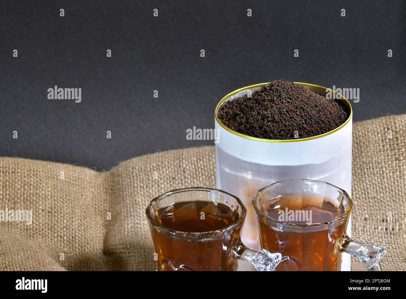 Present two cups of black tea and garden-fresh organic tea leaves in a beautifully designed can - ideal for advertising, packaging Stock Photo