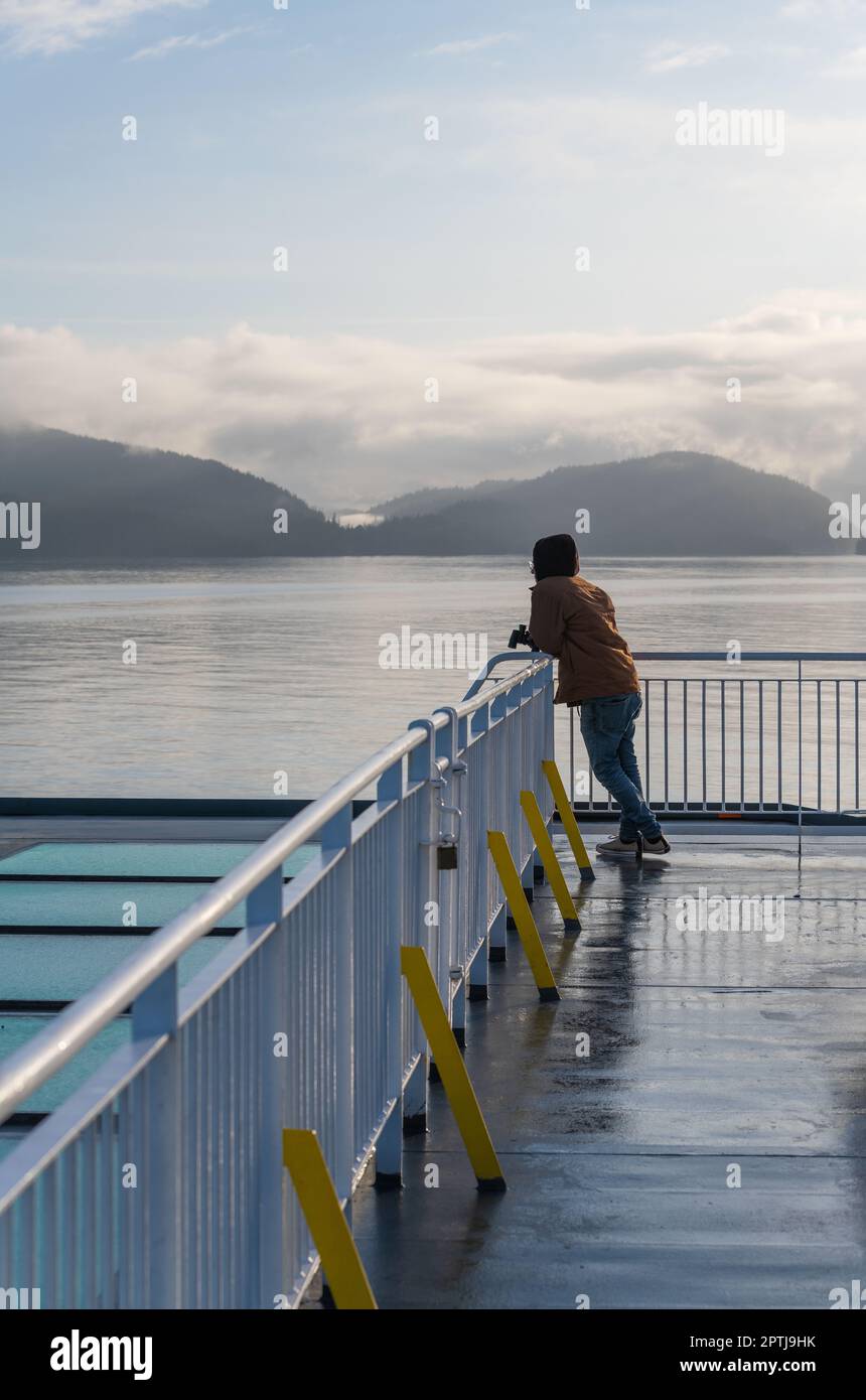 Unrecognizable tourist with binoculars at sunrise on ferry of the Inside Passage cruise near Prince Rupert, British Columbia, Canada. Stock Photo