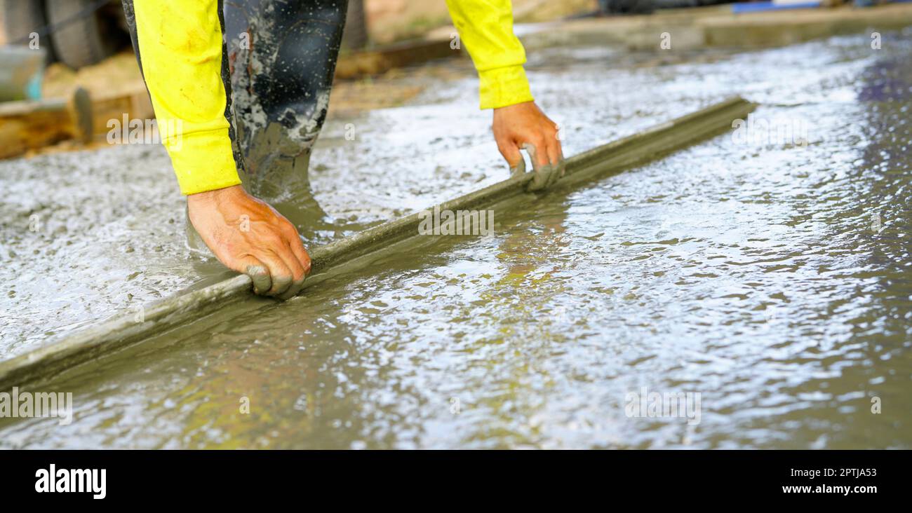 Construction worker leveling wet concrete floor with a trowel at