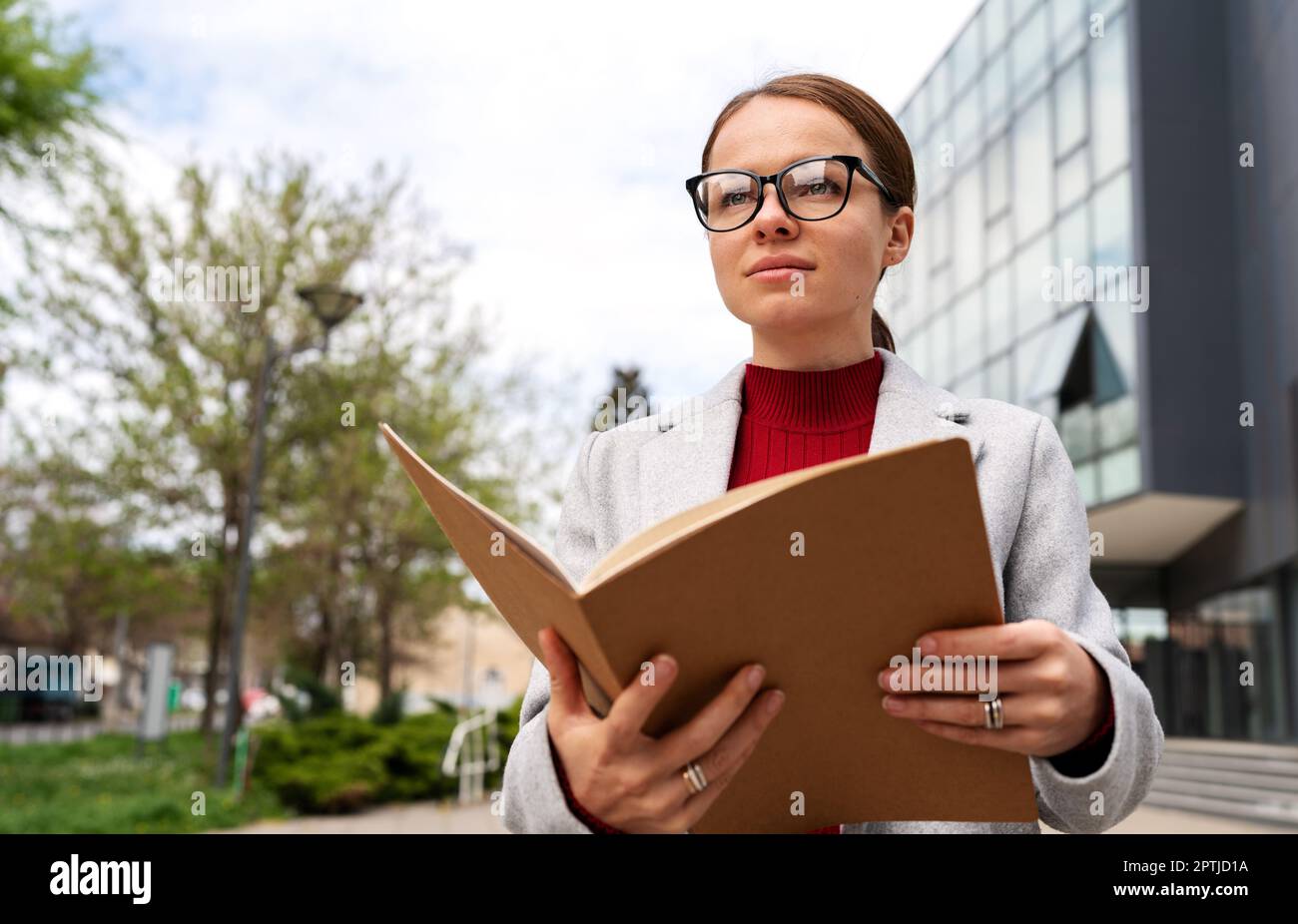 Young adult businesswoman with glasses holding folder with documentation in her hands. Stock Photo