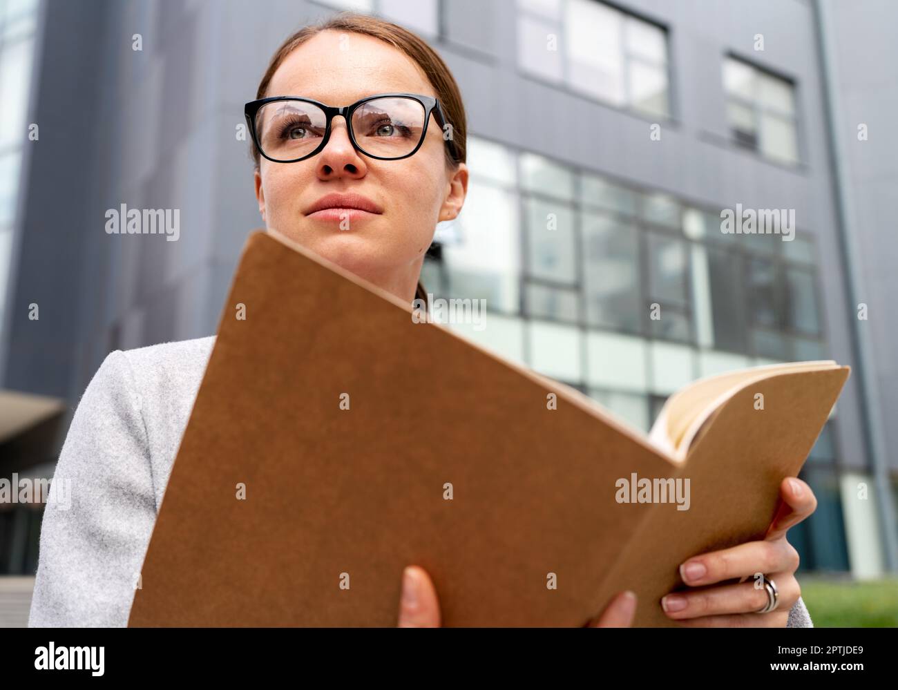 Portrait businesswoman wearing glasses holds folder with documentation in her hands and looking away. Stock Photo