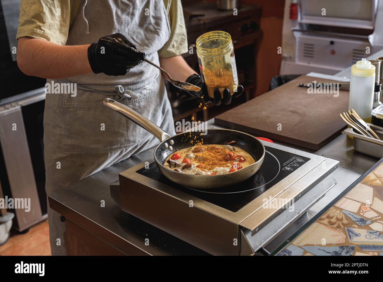 The professional chef in uniform adds spices into pan with dish in ...