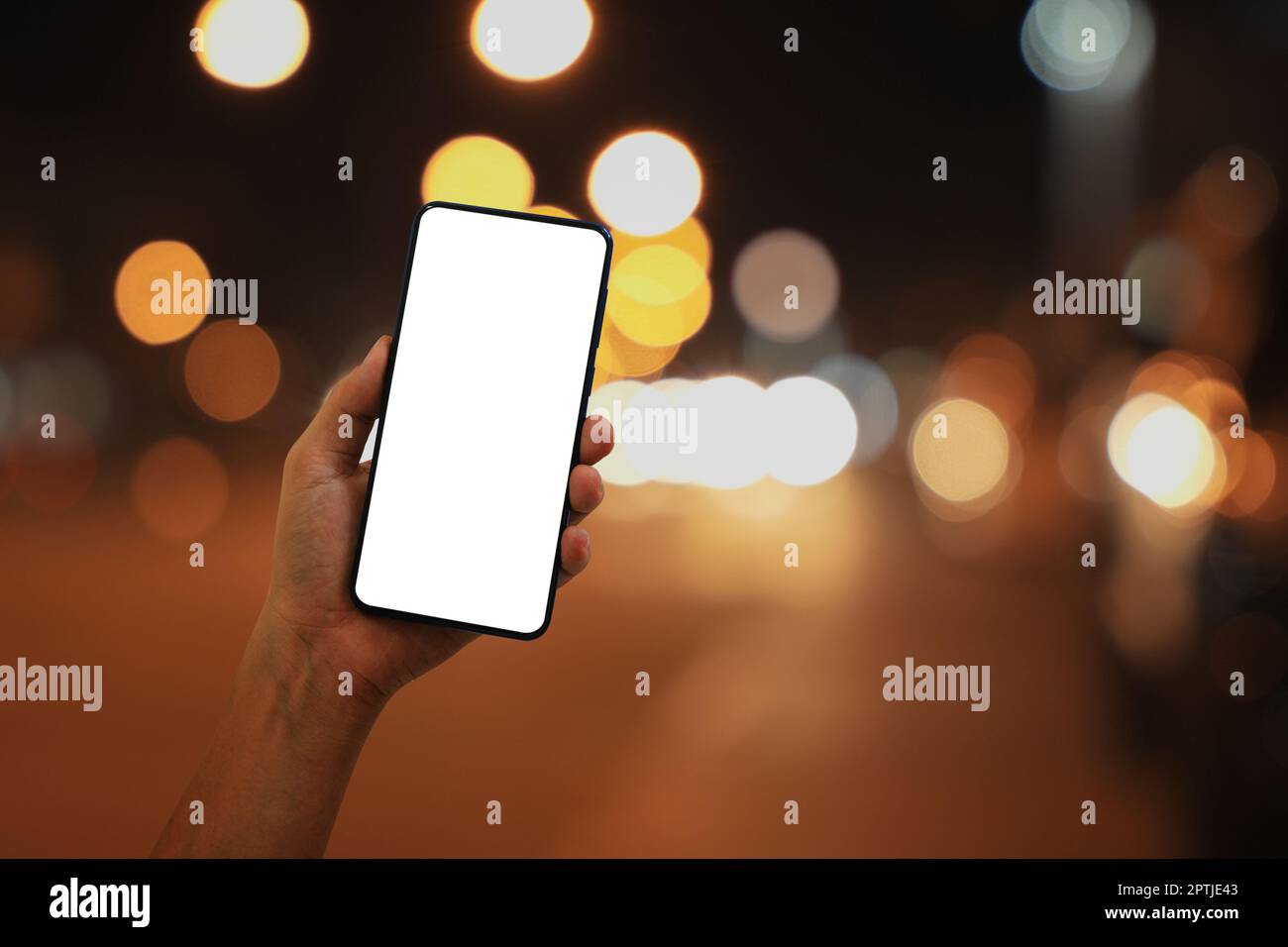 Hand holding smartphone with blank screen at night on bokeh city street ...