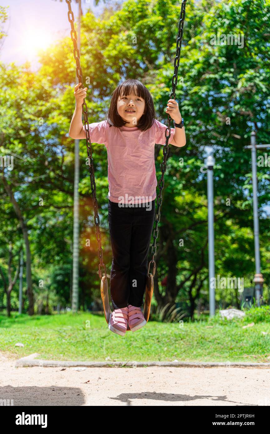 Cute little girl having fun on a swing in beautiful summer garden. Child girl playing on outdoor playground in park. Active summer leisure for kids Stock Photo