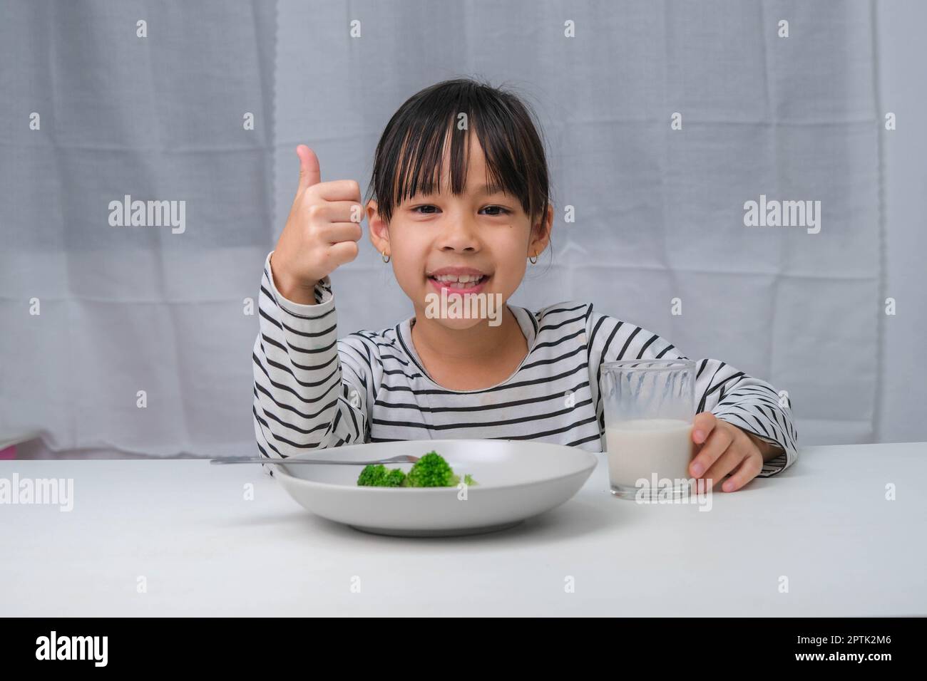 Cute Asian girl drinking a glass of milk in the morning before going to