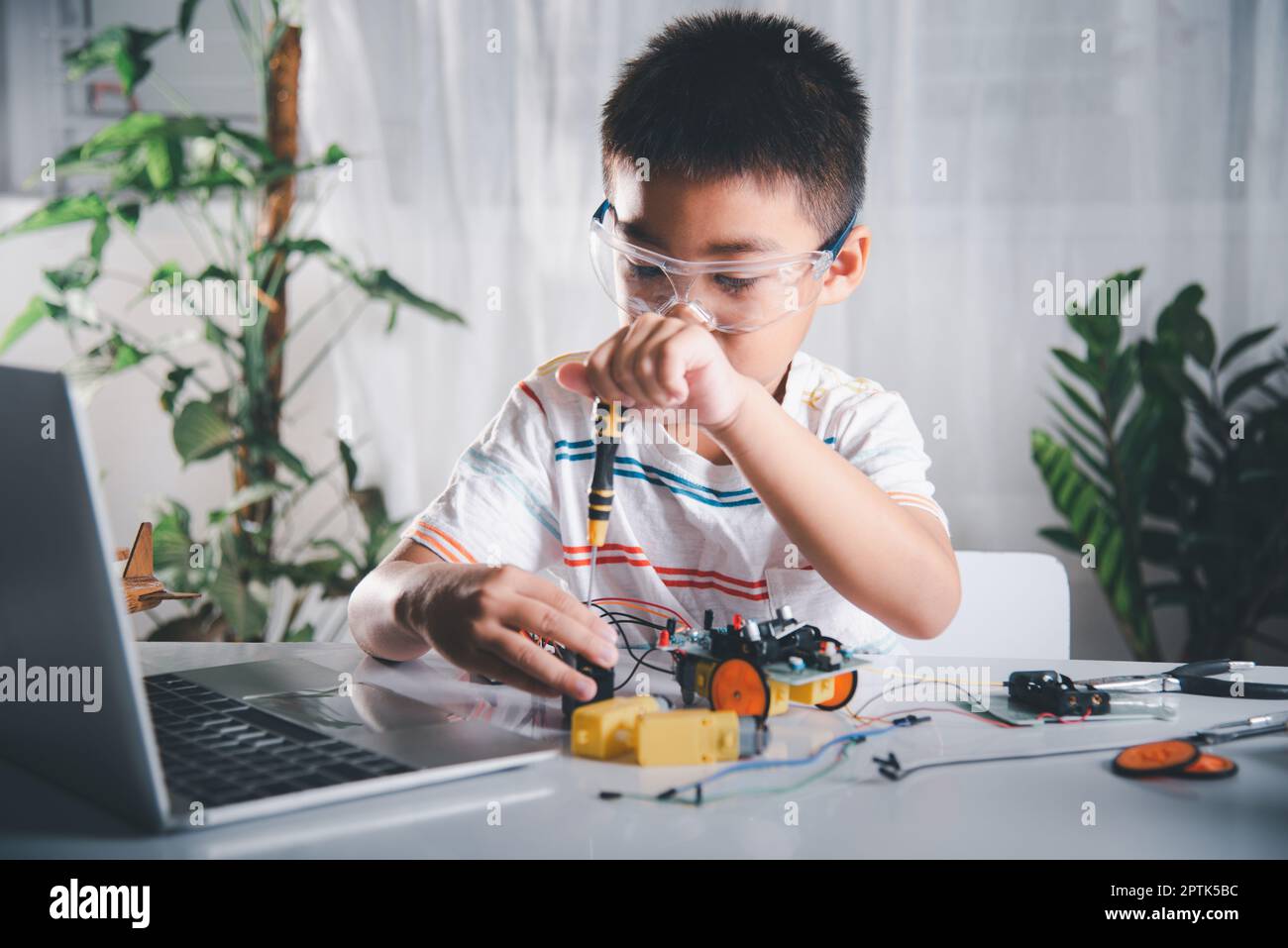 Little child tighten the nut with a screwdriver to assemble car toy, Asian kid boy assembling the Arduino robot car homework project at home, educatio Stock Photo