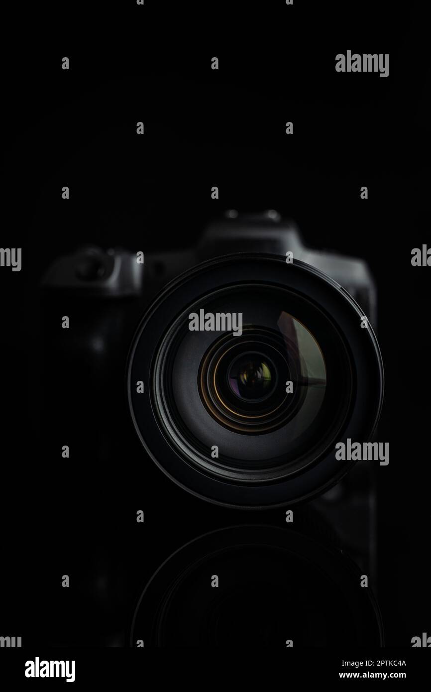 Digital mirrorless camera on the black background. Lens closeup. Front view. Stock Photo