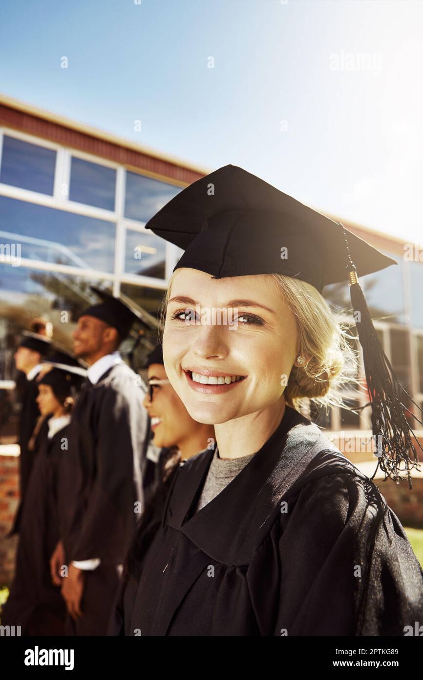 I cant believe I finally graduated. Portrait of a smiling university student on graduation day with classmates in the background. Stock Photo