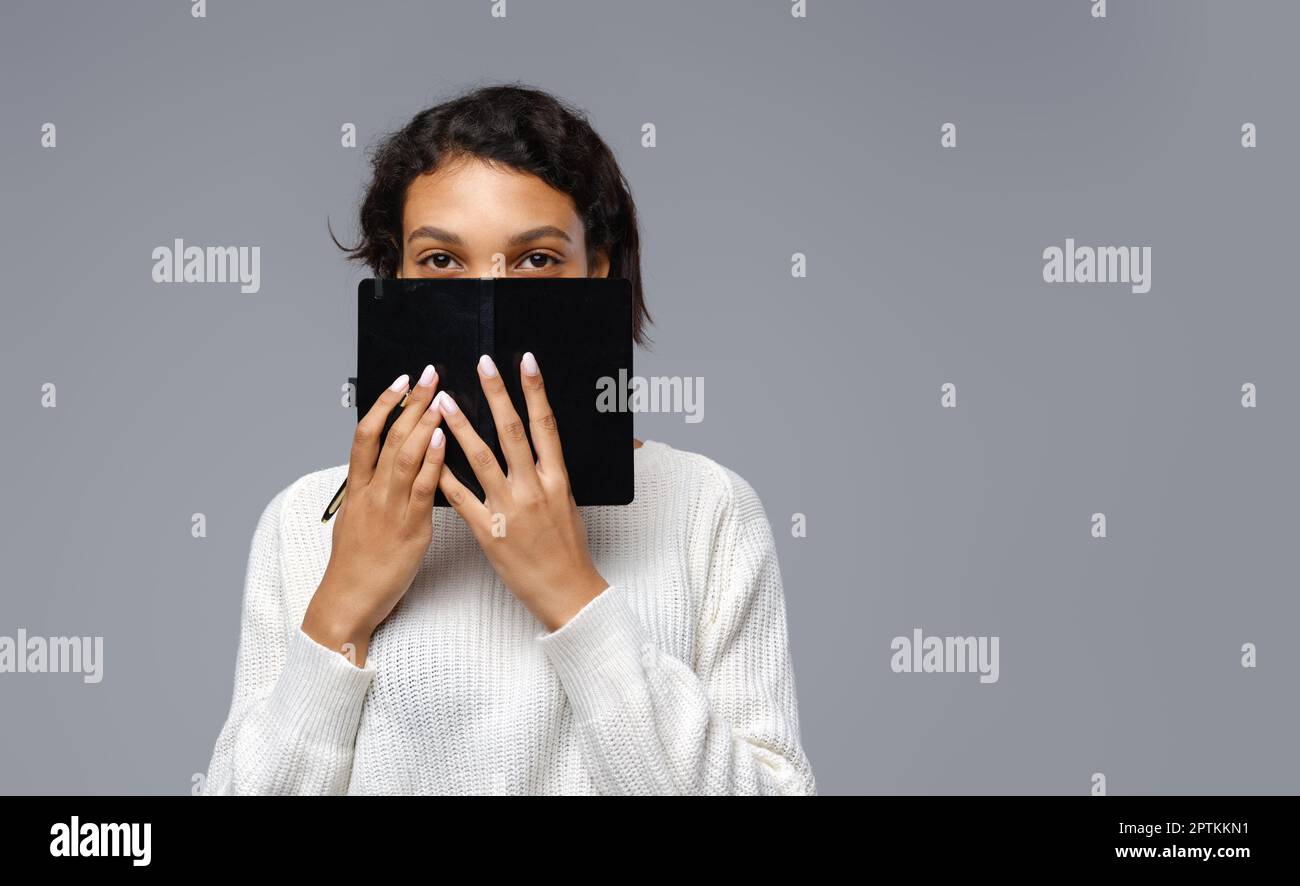Tricky young affican woman hide her face with notebook Stock Photo - Alamy