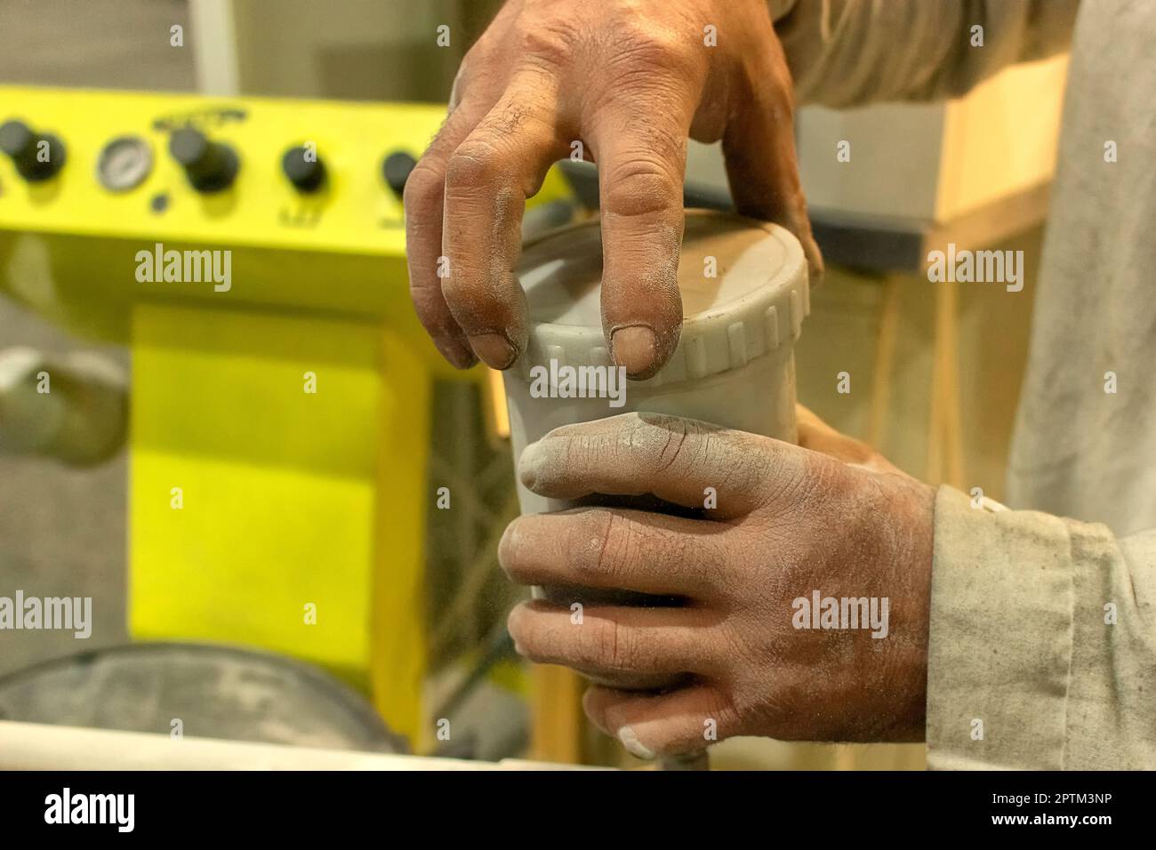 working hands of a white man, a man, in the workshop, in the department of painting metal products, unscrews the lid from a jar of white powder paint. Stock Photo