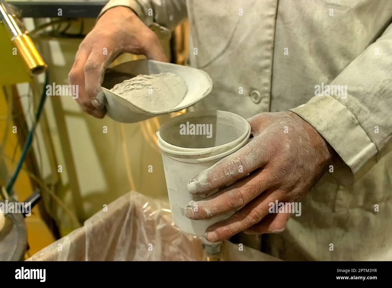 a painting shop, a male worker, manually pours white powder paint into a container, a worker is dressed in special clothes that got dirty during work. Stock Photo
