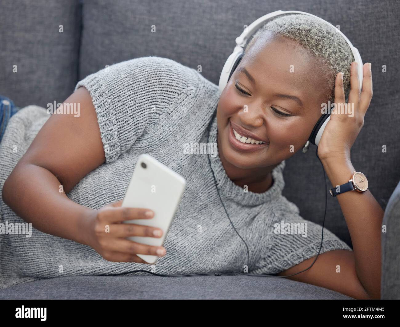 Black woman, music and phone video streaming in a home living room on a sofa happy