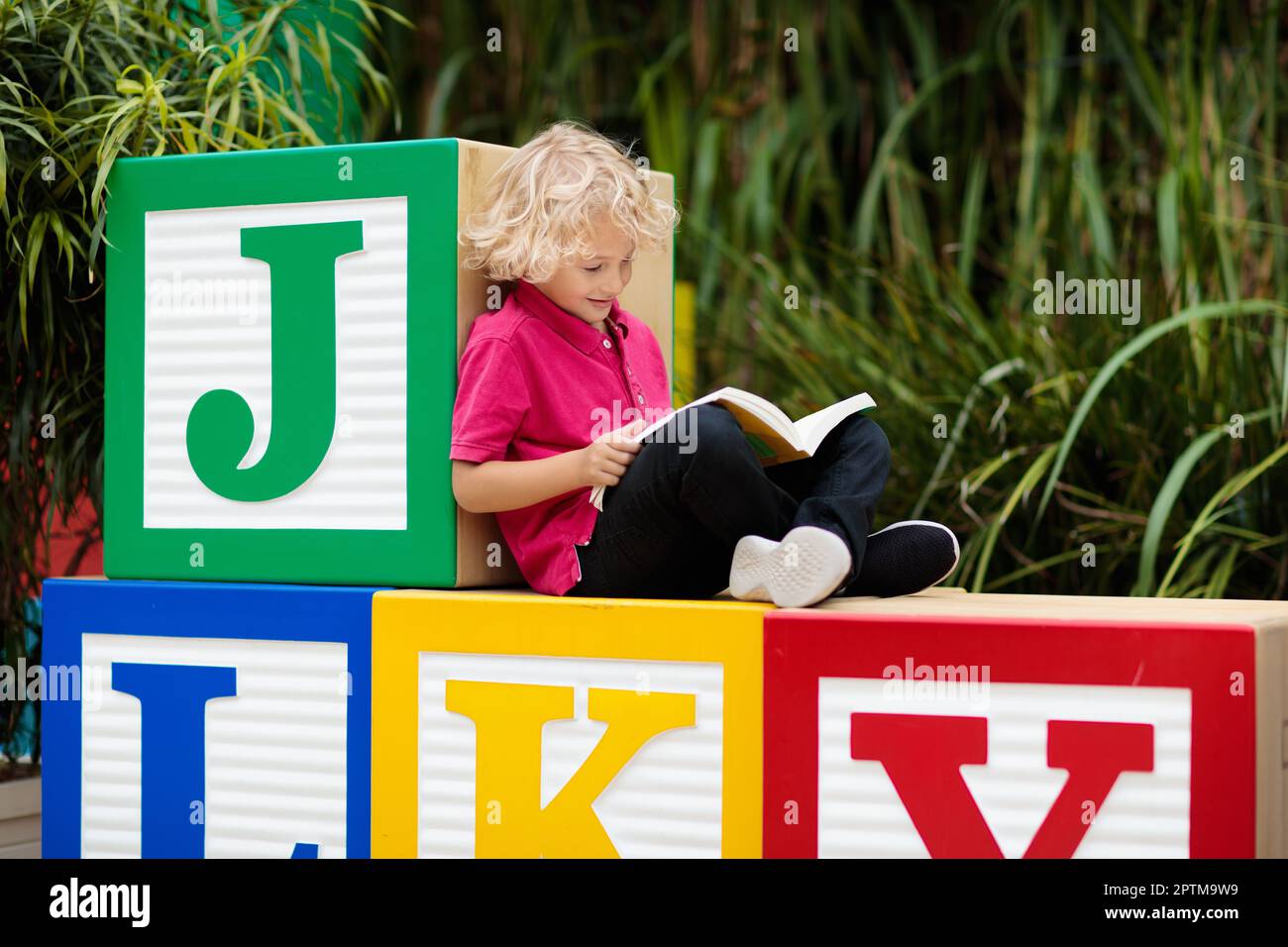 Child reading book in school yard. Kid learning abc letters. Little boy sitting on wooden toy