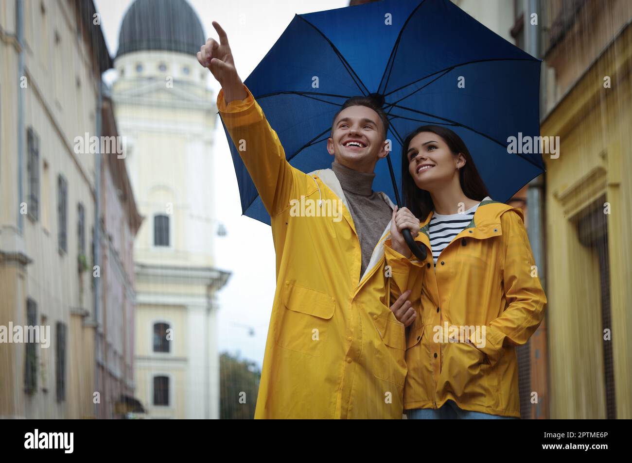 Lovely young couple with umbrella walking under rain on city street ...