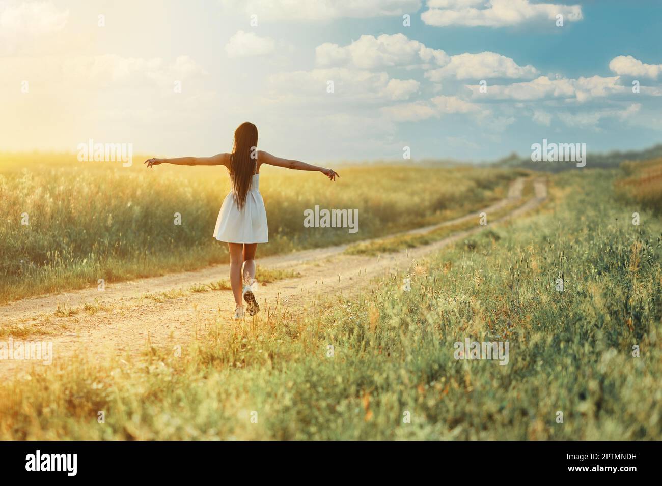 Rear view of a woman walking along country road spreading arms in sides ...