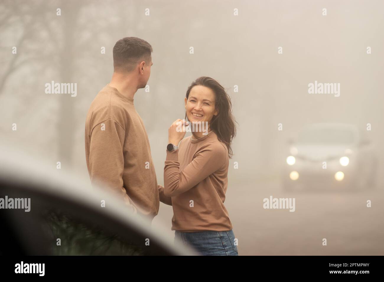 a young heterosexual couple, of white race, on a foggy day, a young woman smiles, a moment of joy, a man watches the traffic on the road, a good mood. Stock Photo