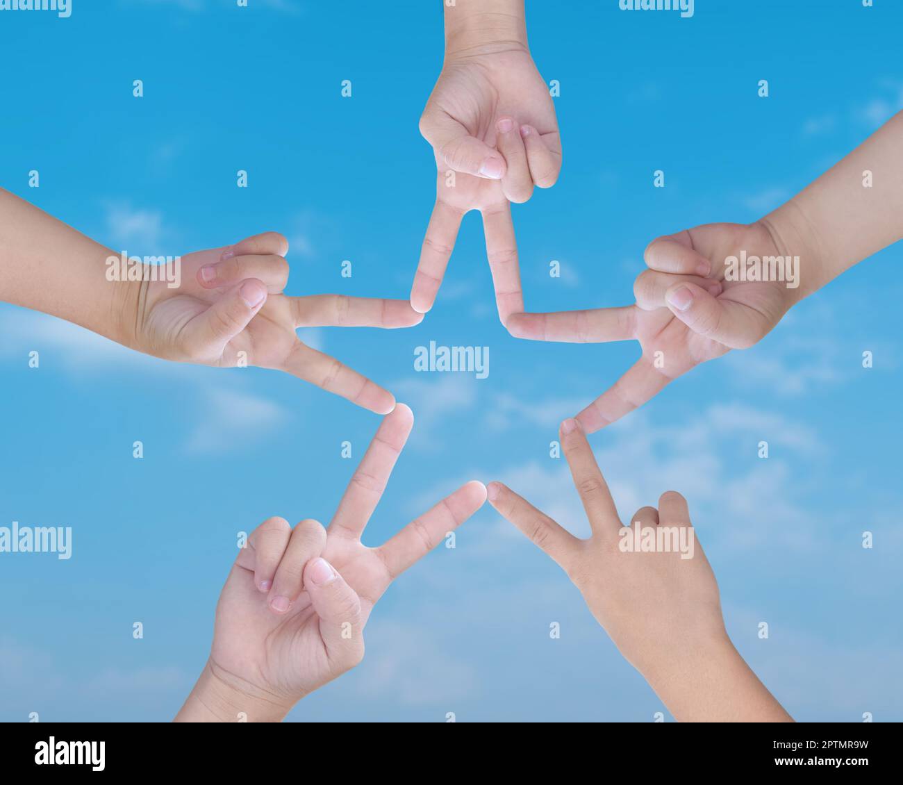 Child hands uniting their to make star shape with fingers, over blue sky background. Conceptual of teamwork. Stock Photo