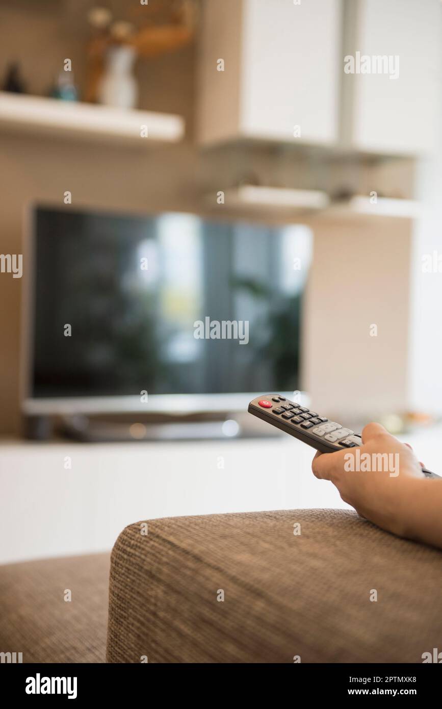 Woman watching TV with remote control in her hand, Munich, Bavaria, Germany Stock Photo