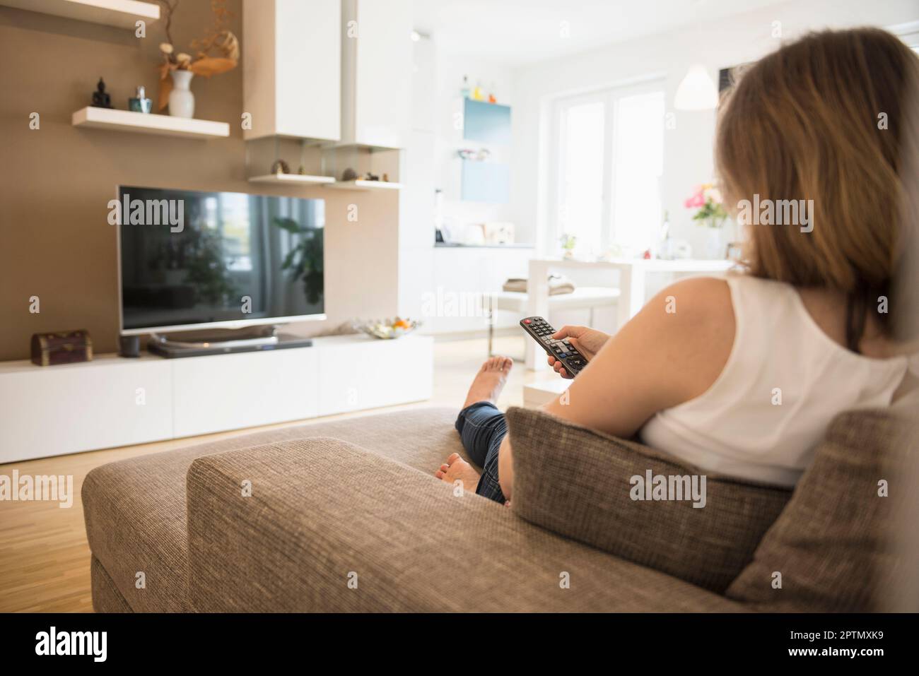 Pregnant woman sitting on sofa and watching TV with remote control, Munich, Bavaria, Germany Stock Photo