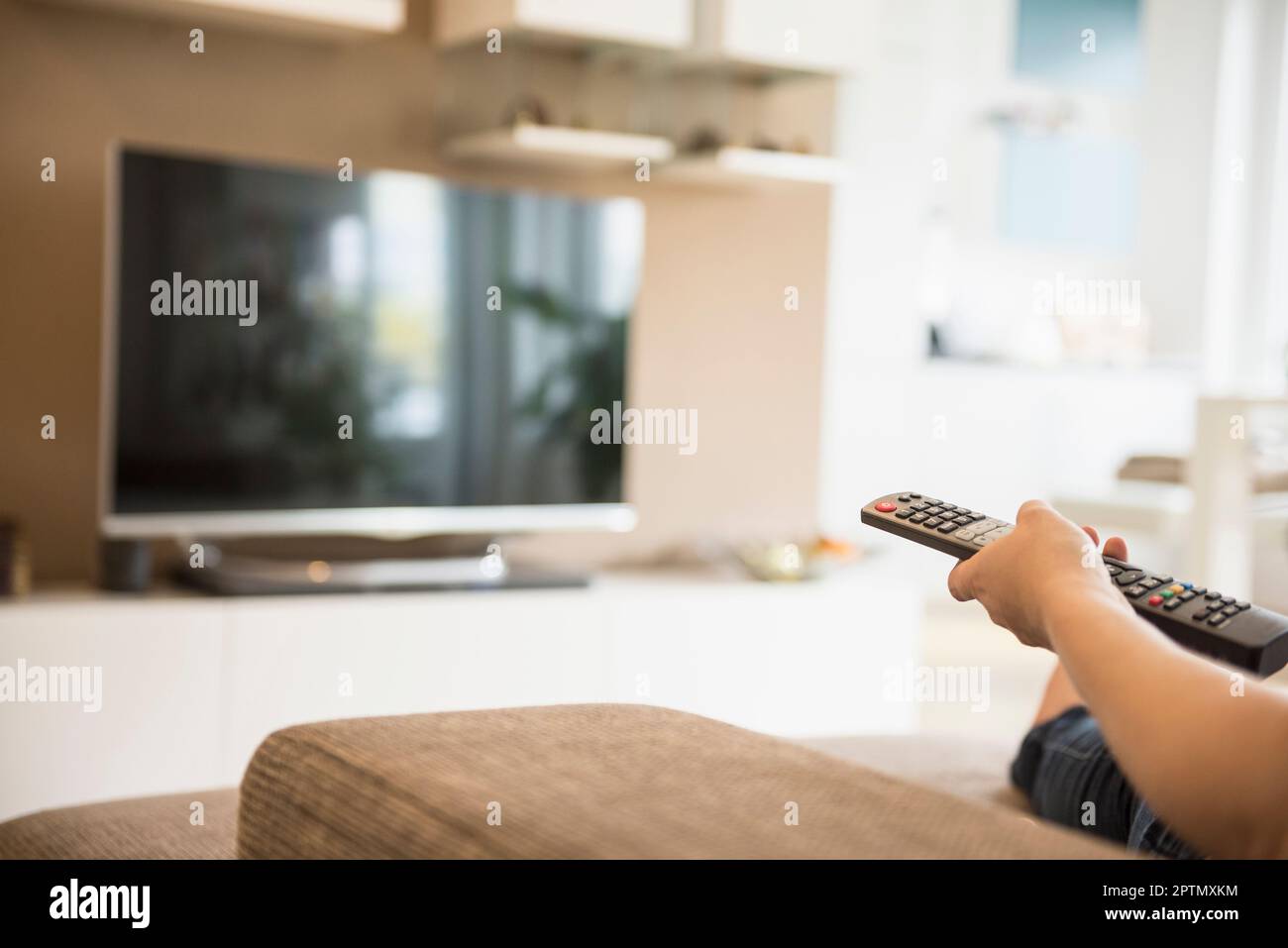 Woman watching TV with remote control in her hand, Munich, Bavaria, Germany Stock Photo