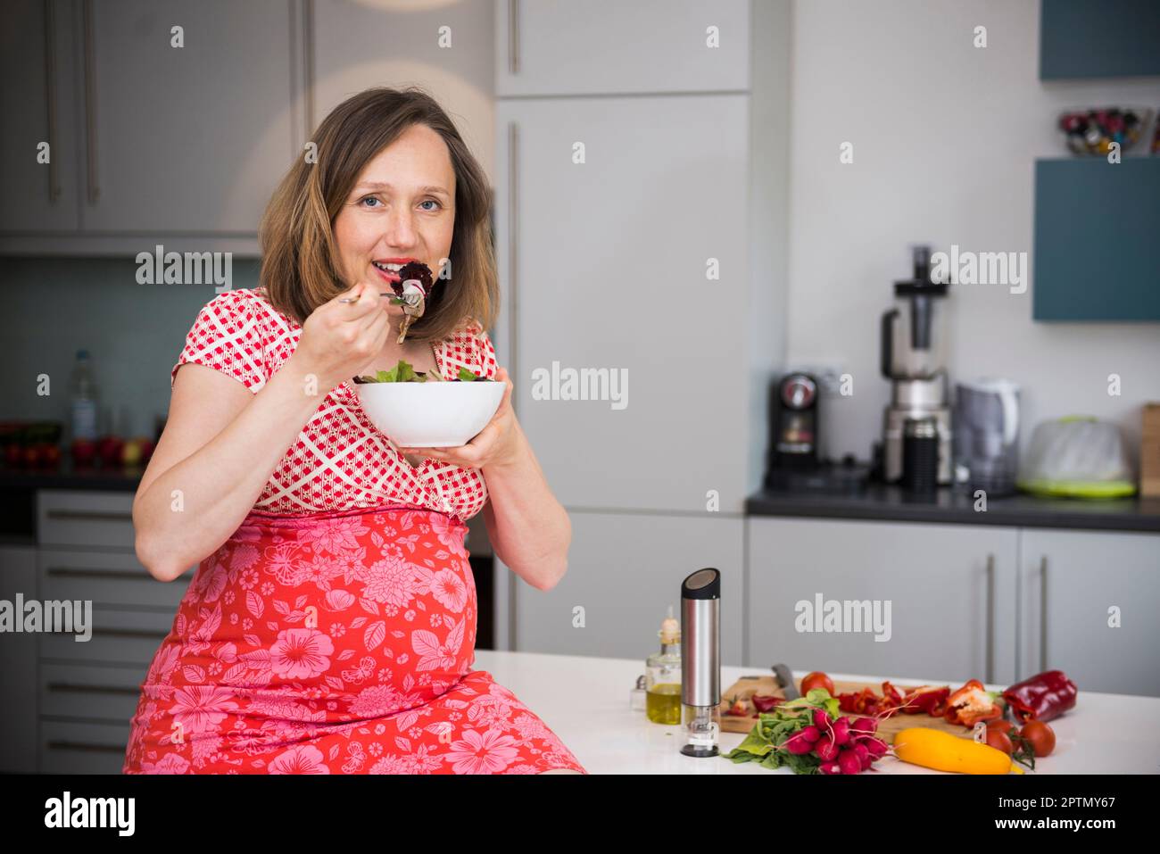 Portrait of a pregnant woman eating salad in the kitchen, Munich, Bavaria, Germany Stock Photo