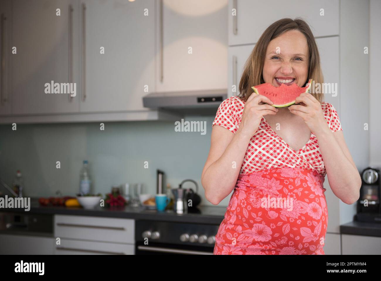 Portrait of a pregnant woman eating watermelon in the kitchen, Munich