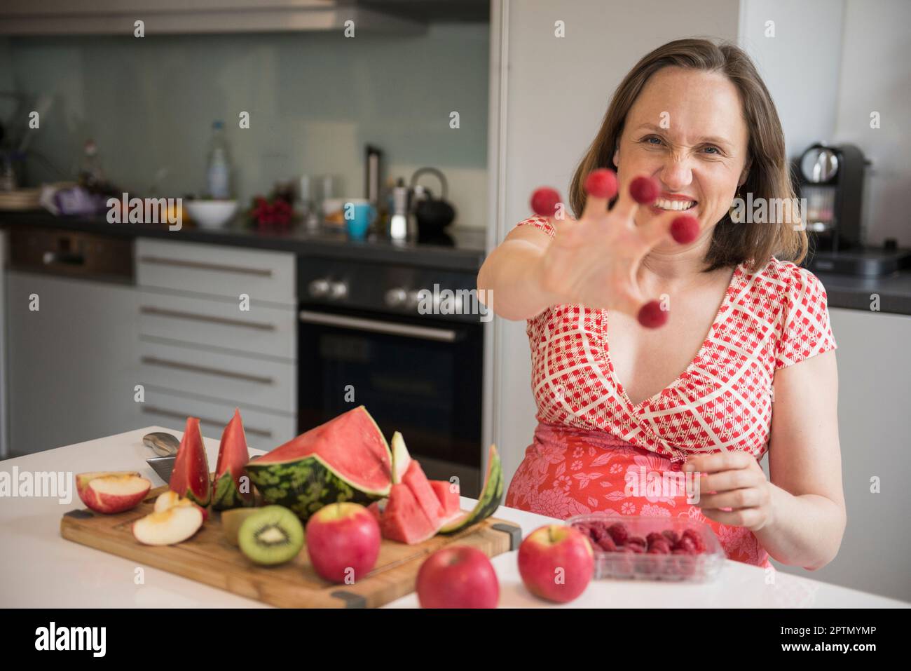 Pregnant woman showing raspberries on her fingers in the kitchen and ...