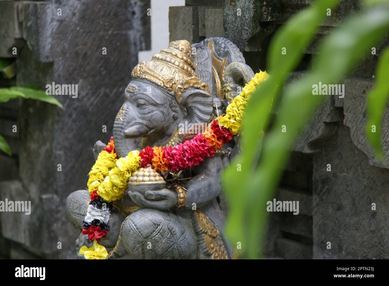Traditional Ganesha statue with flower wreath in Balinese garden. Lord