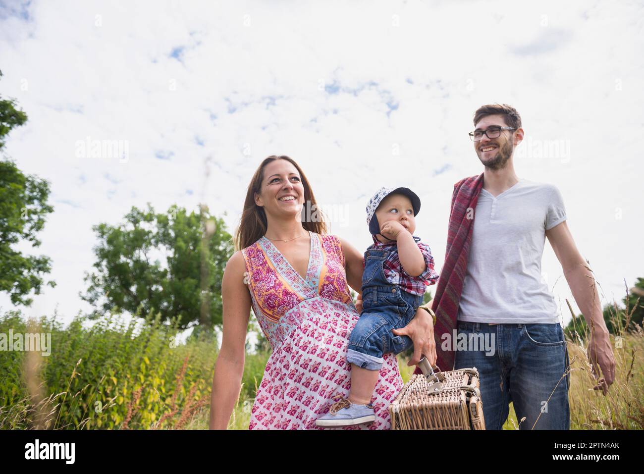 Family with picnic basket walking on meadow and smiling, Bavaria, Germany Stock Photo