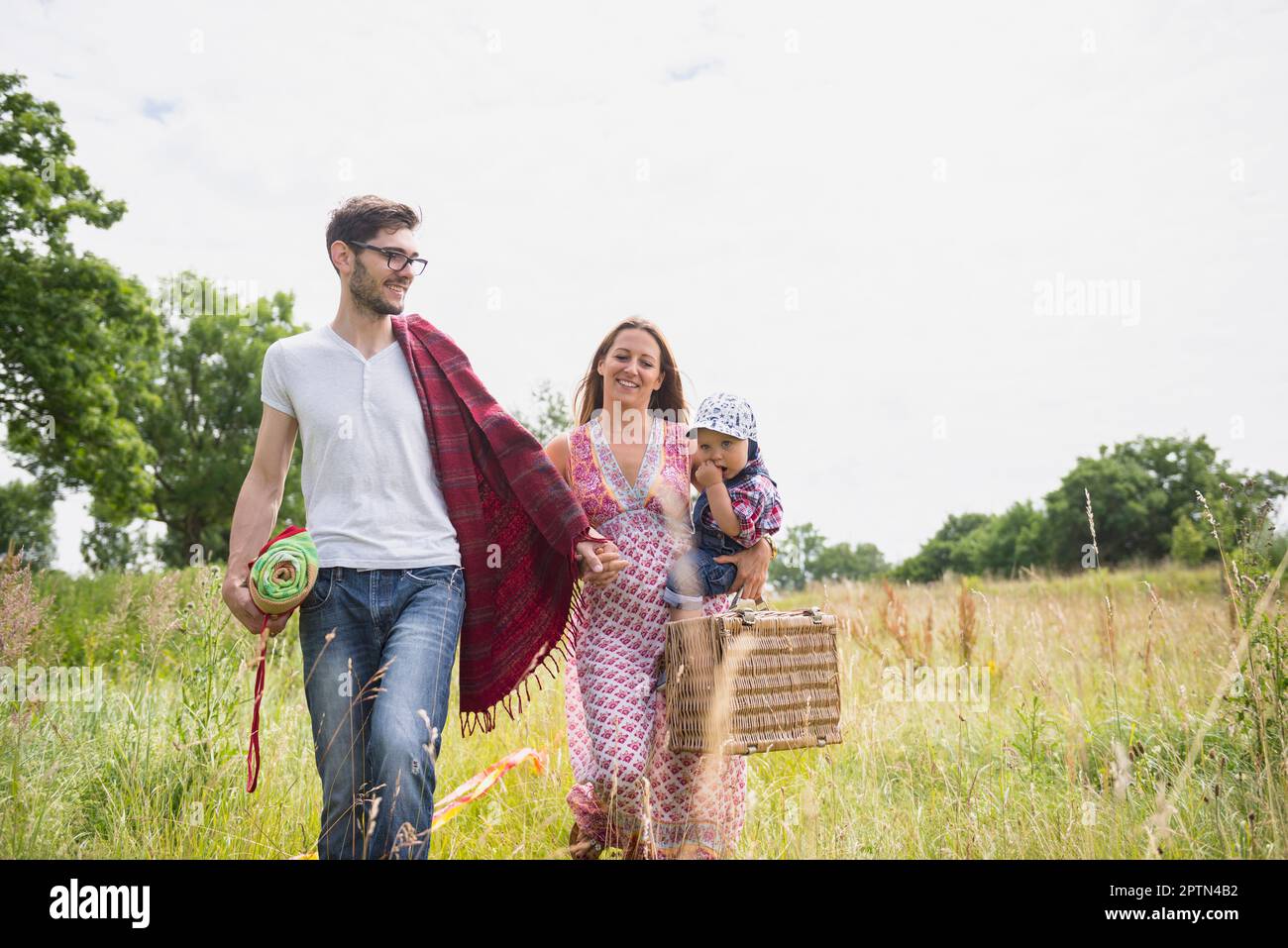 Family with picnic basket walking on meadow and smiling, Bavaria, Germany Stock Photo