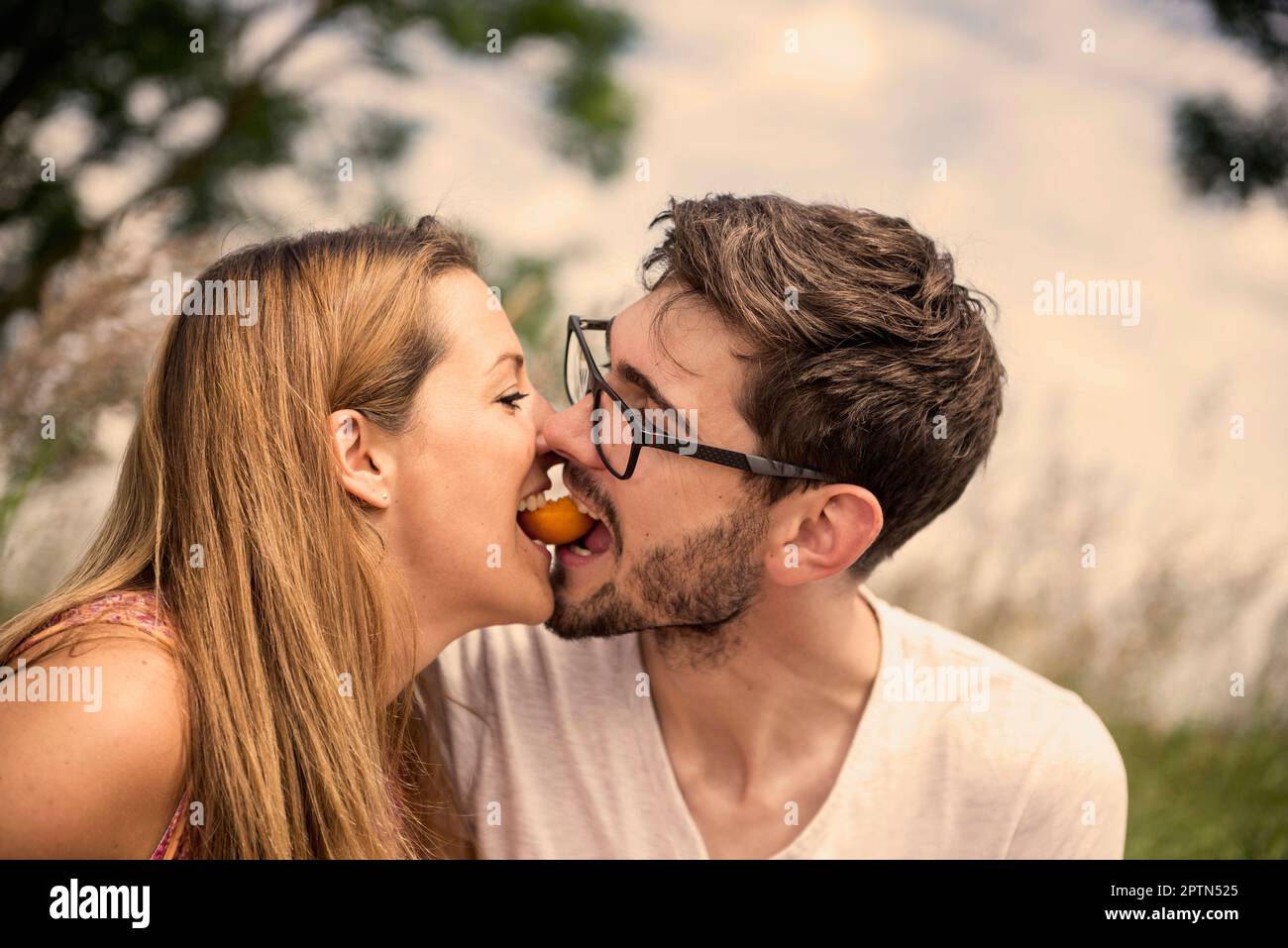 Mid adult couple biting peach together in the countryside, Bavaria, Germany Stock Photo